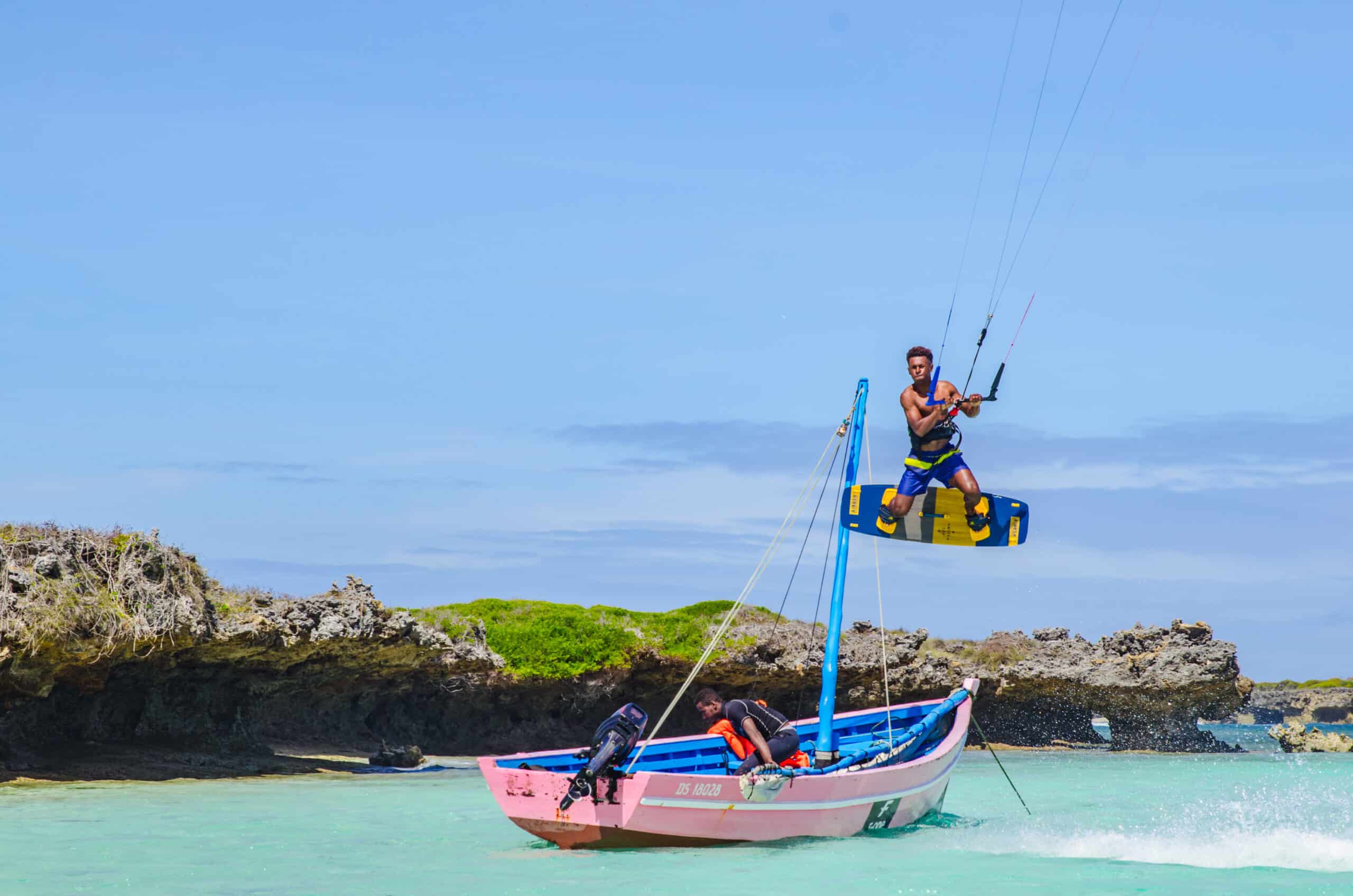 Pirogue colorée et rider de kitesurf en saut près d’un îlot rocheux, Mer d’Émeraude, Madagascar